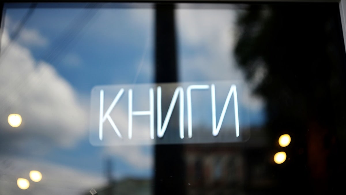 Neon sign 'книги' (books) reflected in a window.